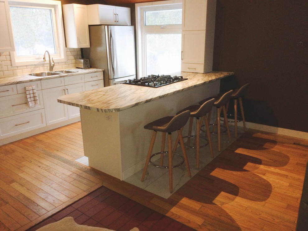 Inspiration for a mid-sized transitional u-shaped light wood floor and brown floor eat-in kitchen remodel with a drop-in sink, raised-panel cabinets, white cabinets, laminate countertops, white backsplash, ceramic backsplash, stainless steel appliances and a peninsula