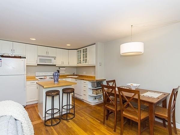 Eat-in kitchen - small rustic medium tone wood floor eat-in kitchen idea in Boston with an undermount sink, flat-panel cabinets, white cabinets, wood countertops, white backsplash, white appliances and an island