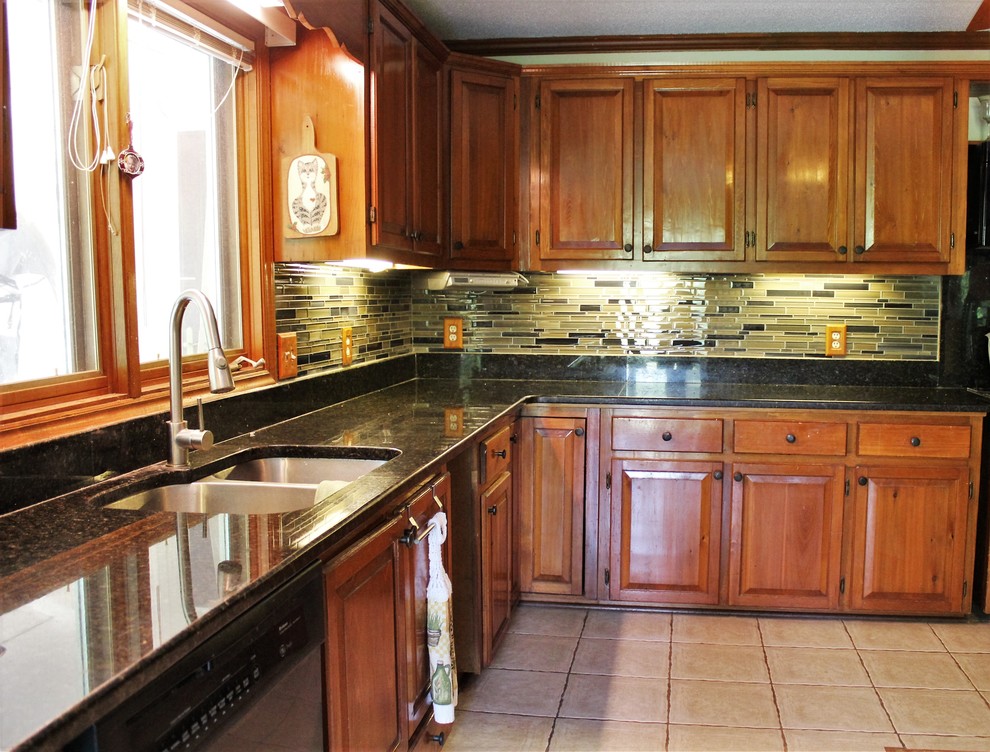 Inspiration for a mid-sized rustic l-shaped ceramic tile enclosed kitchen remodel in Raleigh with a double-bowl sink, raised-panel cabinets, medium tone wood cabinets, granite countertops, multicolored backsplash, glass sheet backsplash, black appliances and no island