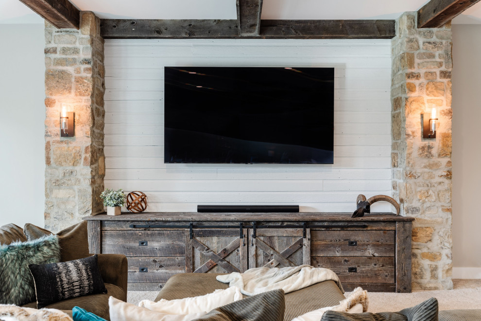 This is an example of a country open concept family room in Omaha with carpet, no fireplace, a stone fireplace surround, a wall-mounted tv, beige floor, exposed beam and planked wall panelling.