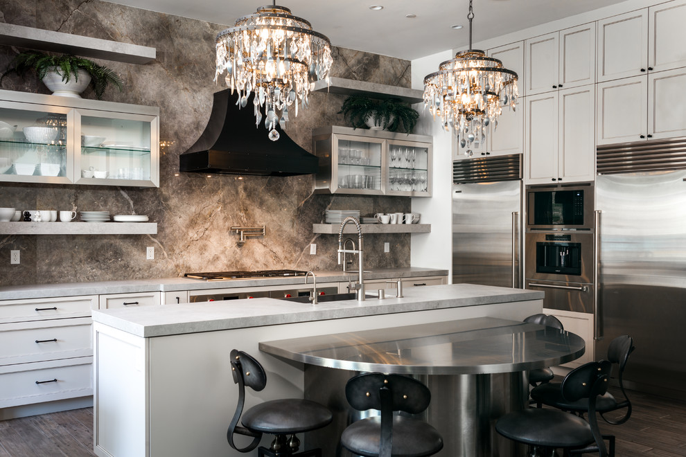 Photo of an eclectic l-shaped kitchen in Los Angeles with a farmhouse sink, shaker cabinets, beige cabinets, grey splashback, marble splashback, stainless steel appliances, dark hardwood floors, with island and grey benchtop.