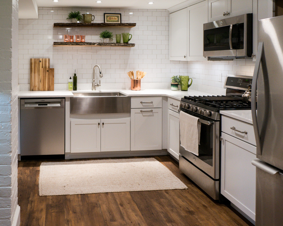 Small eclectic l-shaped kitchen in DC Metro with a farmhouse sink, shaker cabinets, white cabinets, quartz benchtops, white splashback, subway tile splashback, stainless steel appliances, no island, brown floor, white benchtop and vinyl floors.