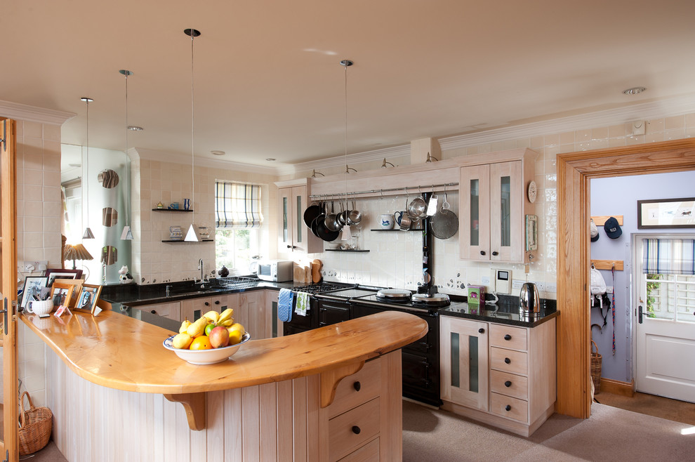 Photo of a mid-sized traditional u-shaped open plan kitchen in London with an integrated sink, shaker cabinets, distressed cabinets, marble benchtops, black splashback, stone tile splashback, black appliances, carpet and no island.