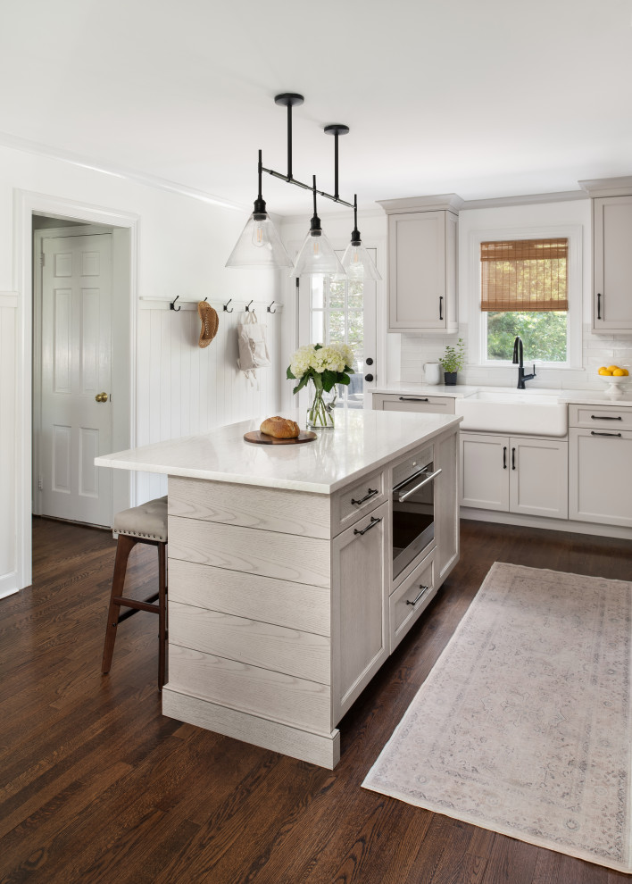 Eat-in kitchen - mid-sized transitional l-shaped medium tone wood floor and brown floor eat-in kitchen idea in New York with a farmhouse sink, shaker cabinets, beige cabinets, quartz countertops, white backsplash, porcelain backsplash, paneled appliances, an island and white countertops