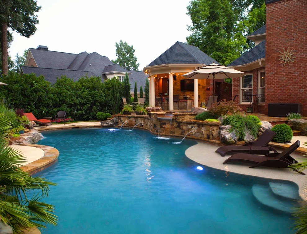 Photo of a mid-sized arts and crafts backyard custom-shaped lap pool in Other with a hot tub and natural stone pavers.