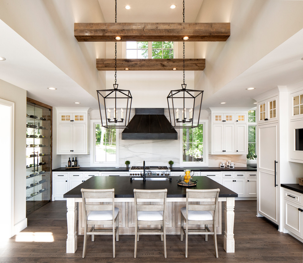 Design ideas for a country u-shaped kitchen in Minneapolis with an undermount sink, recessed-panel cabinets, white cabinets, white splashback, stone slab splashback, panelled appliances, dark hardwood floors, with island, brown floor, black benchtop, exposed beam and vaulted.