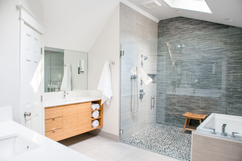 Large transitional master bathroom in Portland Maine with flat-panel cabinets, pebble tile, an undermount sink, light wood cabinets, an alcove shower, a two-piece toilet, white walls, ceramic floors, gray tile, an undermount tub and a hinged shower door.