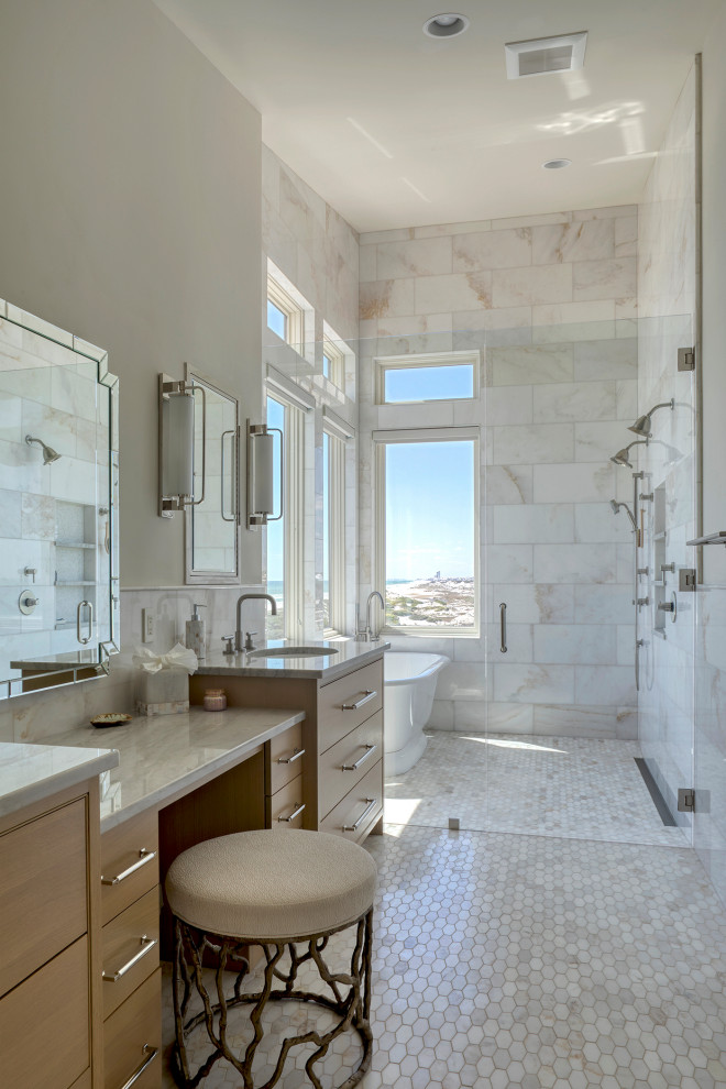 Photo of a large beach style master wet room bathroom in Other with furniture-like cabinets, brown cabinets, a freestanding tub, a one-piece toilet, white walls, ceramic floors, a drop-in sink, marble benchtops, beige floor, a hinged shower door, grey benchtops, a double vanity, a built-in vanity, white tile and marble.