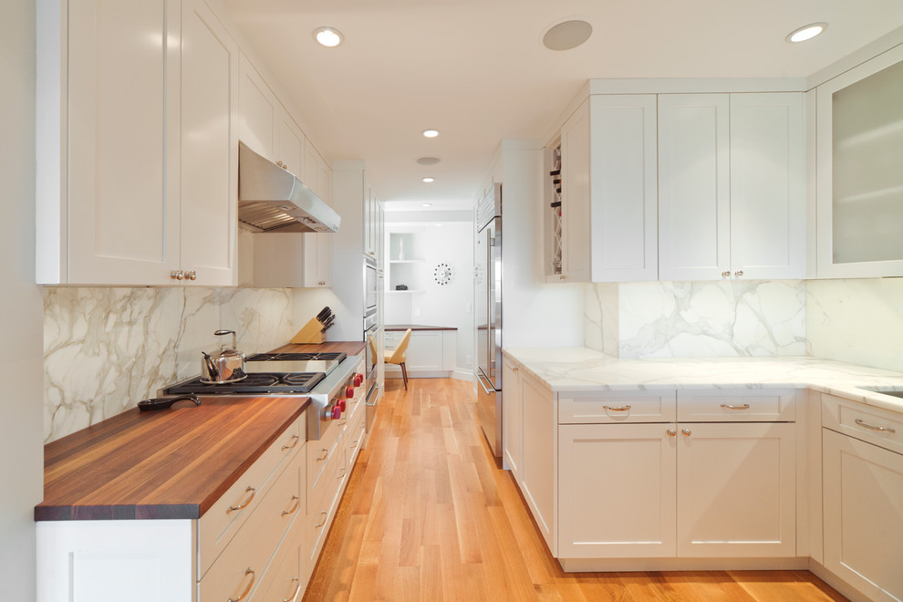 Photo of a mid-sized contemporary galley separate kitchen in New York with shaker cabinets, white cabinets, white splashback, stone slab splashback, light hardwood floors, no island, an undermount sink, marble benchtops, stainless steel appliances and beige floor.
