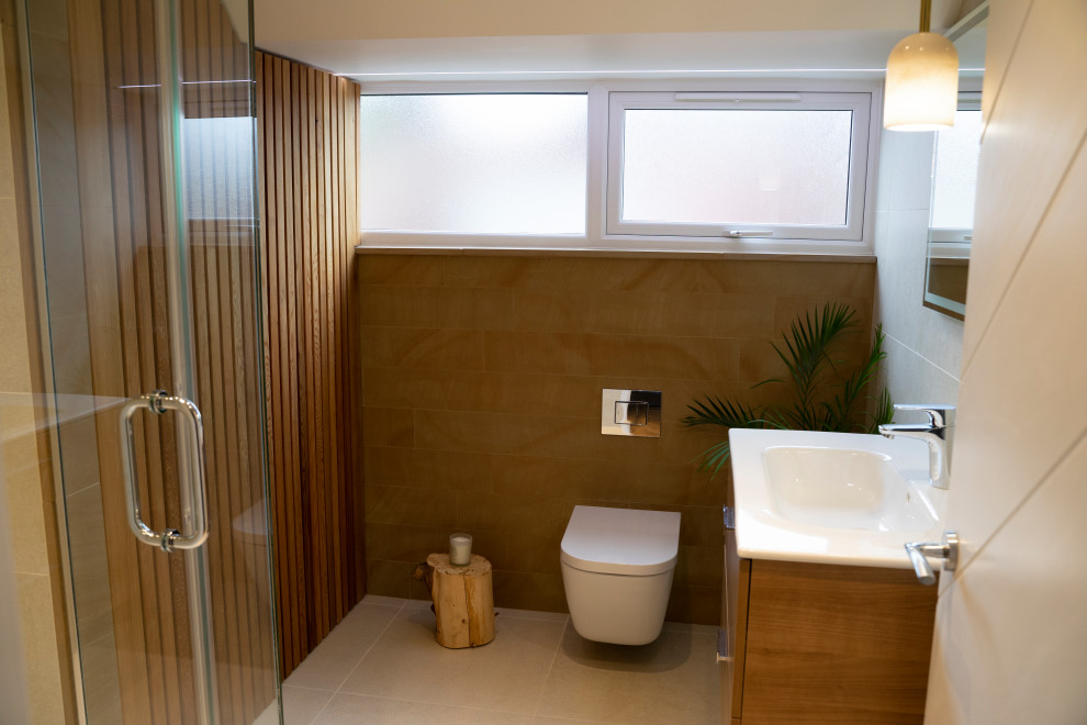 Mid-sized scandinavian 3/4 bathroom in Surrey with brown cabinets, an open shower, a wall-mount toilet, beige tile, ceramic tile, brown walls, cement tiles, a wall-mount sink, beige floor, a hinged shower door, a laundry, a single vanity, a freestanding vanity and wood walls.