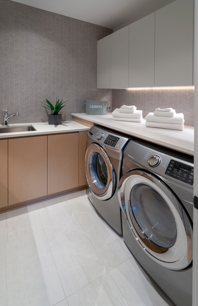 Inspiration for a large contemporary galley dedicated laundry room in Vancouver with an undermount sink, flat-panel cabinets, light wood cabinets, quartz benchtops, grey splashback, mosaic tile splashback, grey walls, porcelain floors, a side-by-side washer and dryer, white floor and white benchtop.