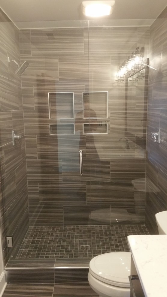 Inspiration for a mid-sized transitional 3/4 brown tile and porcelain tile porcelain tile and brown floor alcove shower remodel with flat-panel cabinets, brown cabinets, a two-piece toilet, white walls, an undermount sink, solid surface countertops, a hinged shower door and white countertops