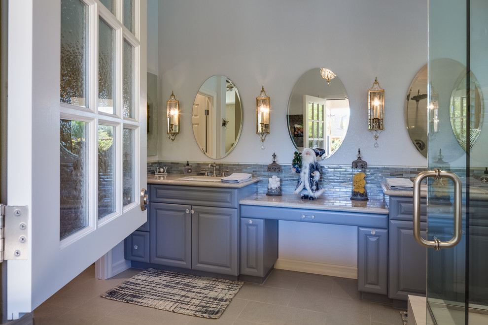 This is an example of a mid-sized transitional master bathroom in San Diego with shaker cabinets, blue cabinets, a corner shower, gray tile, porcelain tile, blue walls, porcelain floors, an undermount sink and marble benchtops.