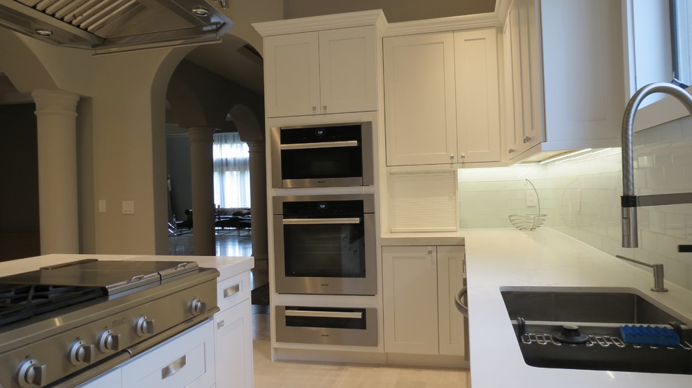 Large transitional l-shaped light wood floor and beige floor enclosed kitchen photo with a double-bowl sink, shaker cabinets, white cabinets, marble countertops, blue backsplash, glass tile backsplash, stainless steel appliances and an island