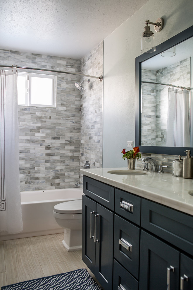 Photo of a small beach style bathroom in Los Angeles with shaker cabinets, blue cabinets, an alcove tub, a shower/bathtub combo, gray tile, glass tile, grey walls, porcelain floors, an undermount sink and granite benchtops.