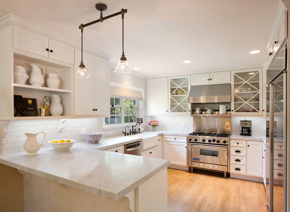 This is an example of a traditional kitchen in Houston with glass-front cabinets, stainless steel appliances, subway tile splashback, a farmhouse sink, marble benchtops and white splashback.