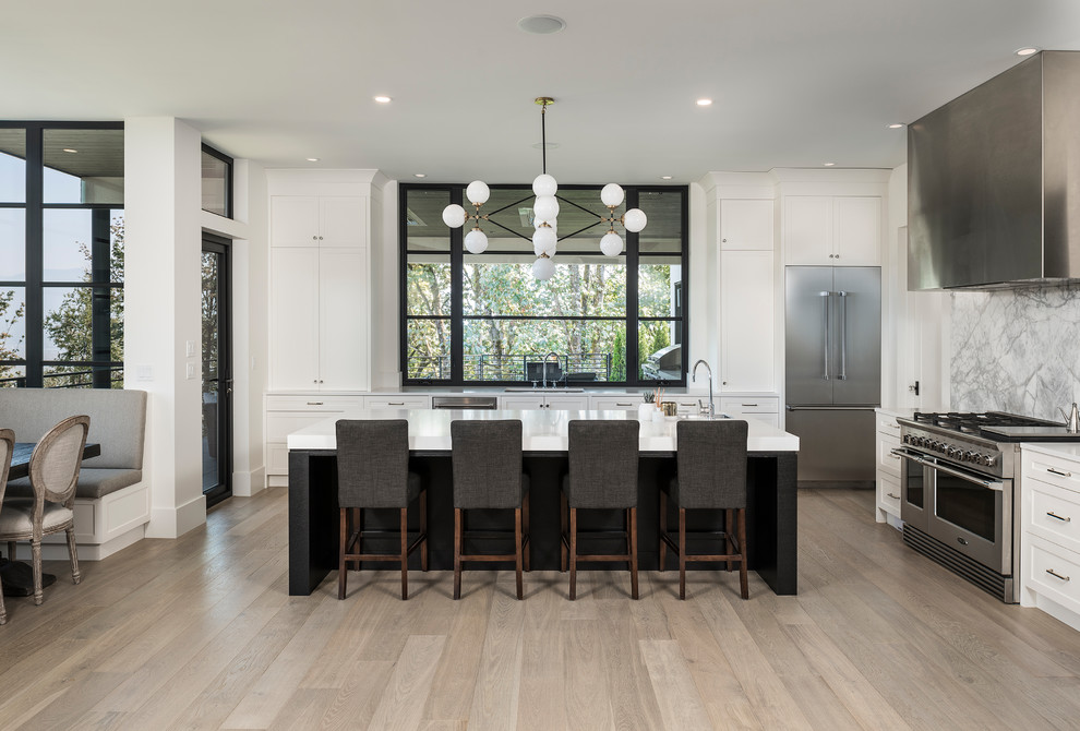 Design ideas for a large contemporary open plan kitchen in Vancouver with shaker cabinets, white splashback, marble splashback, stainless steel appliances, light hardwood floors, with island, white benchtop and an undermount sink.