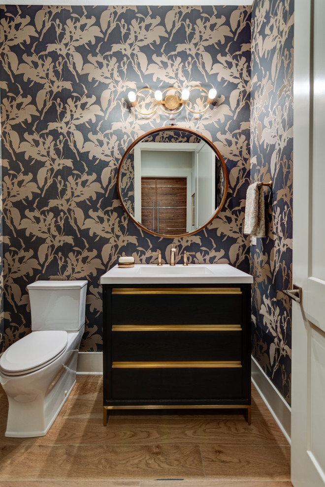 Photo of a mid-sized contemporary powder room in Indianapolis with furniture-like cabinets, black cabinets, a two-piece toilet, black walls, light hardwood floors, an integrated sink, engineered quartz benchtops, brown floor, white benchtops and a freestanding vanity.