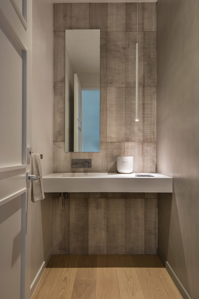 Design ideas for a mid-sized modern 3/4 bathroom in Denver with flat-panel cabinets, beige cabinets, a one-piece toilet, beige tile, marble, white walls, light hardwood floors, an integrated sink, solid surface benchtops, beige floor and white benchtops.