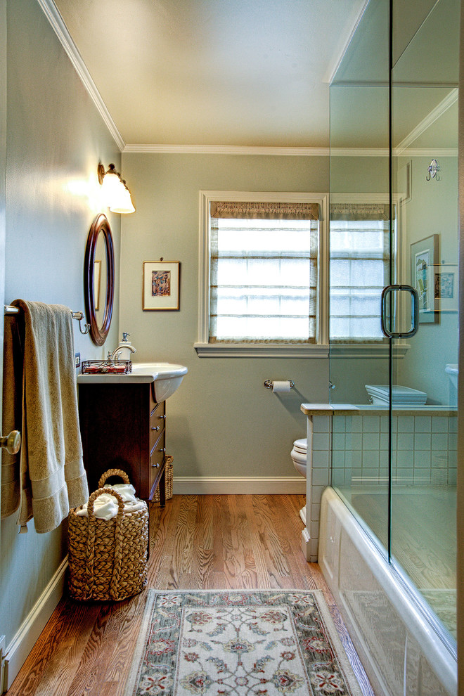 Design ideas for a traditional bathroom in Seattle with an integrated sink, flat-panel cabinets, dark wood cabinets, an alcove tub, a shower/bathtub combo, a two-piece toilet, white tile, porcelain tile, grey walls and medium hardwood floors.