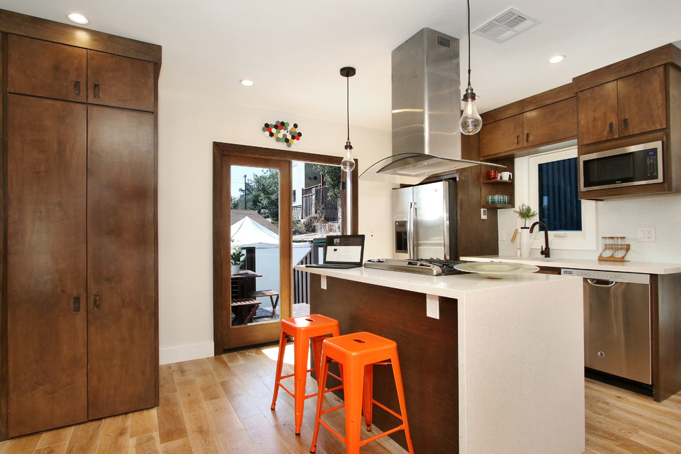 Design ideas for a small eclectic galley open plan kitchen in Los Angeles with a drop-in sink, flat-panel cabinets, dark wood cabinets, quartz benchtops, white splashback, glass tile splashback, stainless steel appliances, light hardwood floors and with island.