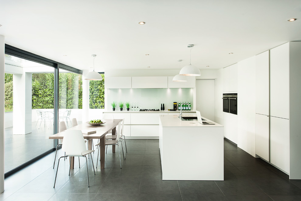 Design ideas for a large modern single-wall eat-in kitchen in Hampshire with flat-panel cabinets, white cabinets, grey floor, an undermount sink, solid surface benchtops, grey splashback, glass sheet splashback, stainless steel appliances and with island.