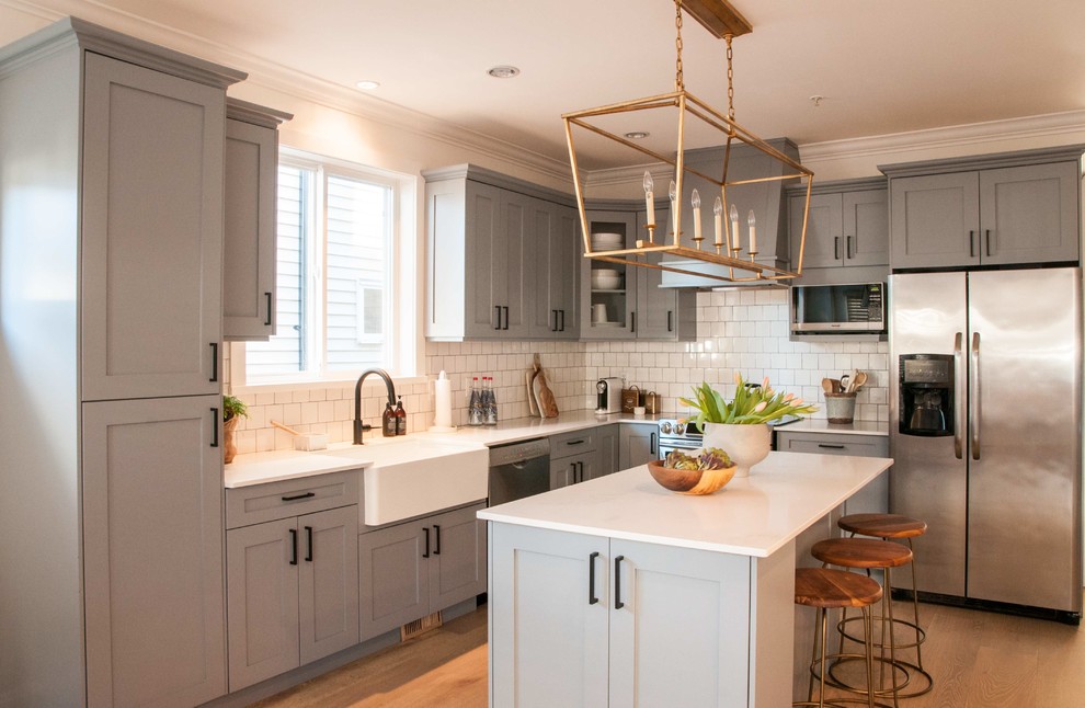 Inspiration for a mid-sized country l-shaped kitchen in Vancouver with a farmhouse sink, raised-panel cabinets, grey cabinets, white splashback, subway tile splashback, stainless steel appliances, medium hardwood floors, with island and brown floor.