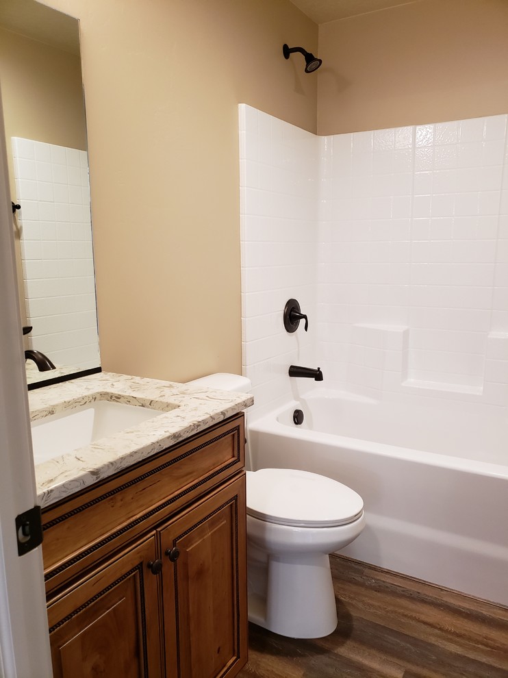 Design ideas for a mid-sized arts and crafts kids bathroom in Other with raised-panel cabinets, medium wood cabinets, an alcove tub, a shower/bathtub combo, a one-piece toilet, beige walls, laminate floors, an undermount sink, engineered quartz benchtops, brown floor, a shower curtain, multi-coloured benchtops and white tile.
