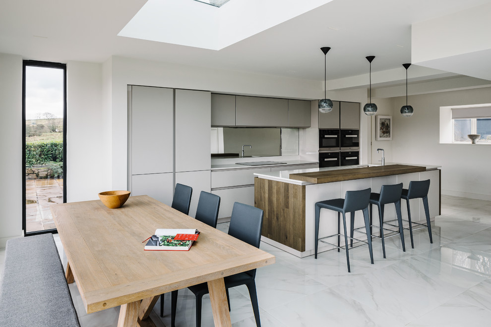 Photo of a mid-sized contemporary galley eat-in kitchen in Manchester with grey cabinets, with island, white benchtop, mirror splashback, an undermount sink, flat-panel cabinets, black appliances, marble floors and grey floor.