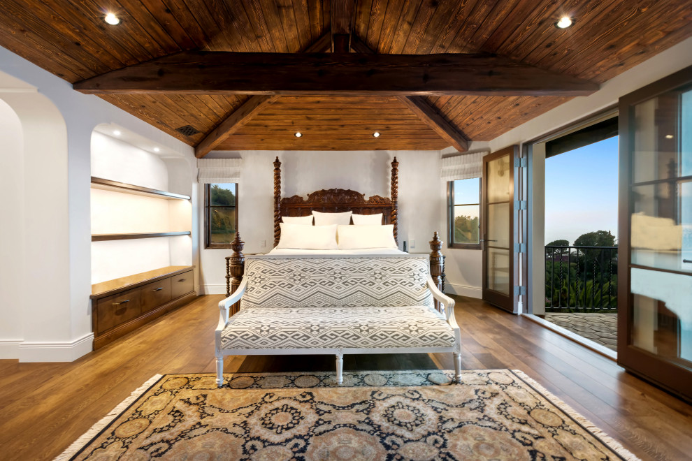 Foto på ett stort medelhavsstil sovrum, med vita väggar, mellanmörkt trägolv, en bred öppen spis, en spiselkrans i trä och brunt golv