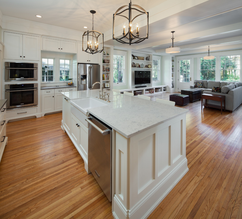 Inspiration for an arts and crafts eat-in kitchen in Charlotte with a farmhouse sink, flat-panel cabinets, white cabinets, marble benchtops, white splashback, subway tile splashback, stainless steel appliances, light hardwood floors and with island.