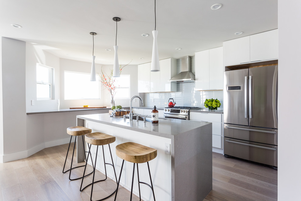 Mid-sized contemporary kitchen in San Francisco with an undermount sink, flat-panel cabinets, white cabinets, white splashback, stainless steel appliances, light hardwood floors, with island, beige floor, quartz benchtops, glass tile splashback and grey benchtop.