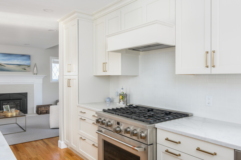 Inredning av ett klassiskt stort vit vitt kök, med en undermonterad diskho, luckor med infälld panel, vita skåp, bänkskiva i kvartsit, vitt stänkskydd, stänkskydd i keramik, rostfria vitvaror, mellanmörkt trägolv, en köksö och brunt golv