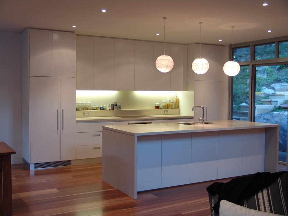 Offene Moderne Küche mit flächenbündigen Schrankfronten, Quarzwerkstein-Arbeitsplatte, Glasrückwand, Küchengeräten aus Edelstahl, zwei Kücheninseln und weißer Arbeitsplatte in Sydney