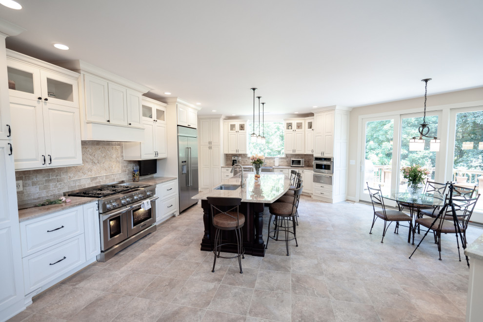Photo of a large traditional l-shaped open plan kitchen in DC Metro with a farmhouse sink, raised-panel cabinets, white cabinets, granite benchtops, beige splashback, travertine splashback, stainless steel appliances, travertine floors, with island, beige floor and beige benchtop.