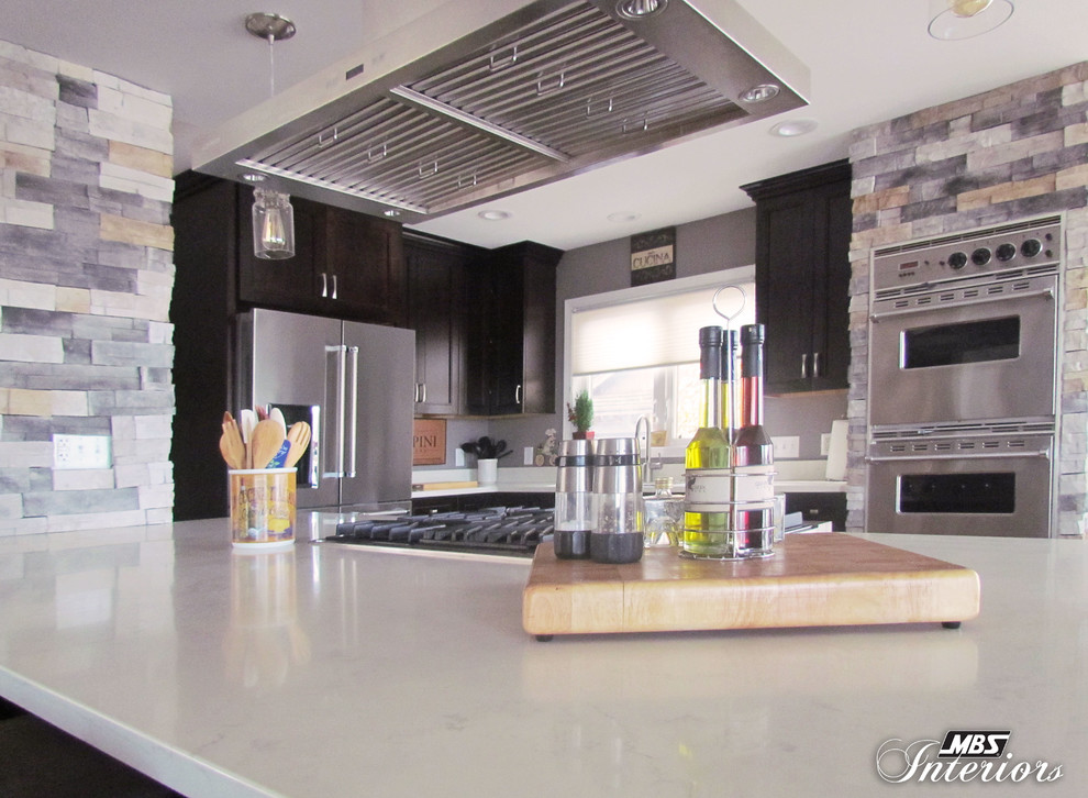 Example of a large transitional l-shaped light wood floor eat-in kitchen design with an undermount sink, recessed-panel cabinets, dark wood cabinets, quartz countertops, stainless steel appliances and an island