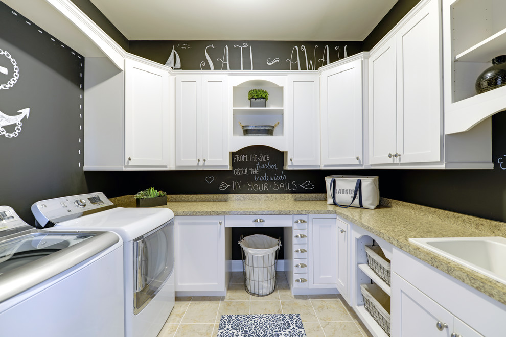 Inspiration for a beach style u-shaped dedicated laundry room in Other with a drop-in sink, recessed-panel cabinets, white cabinets, granite benchtops, black walls, porcelain floors and a side-by-side washer and dryer.