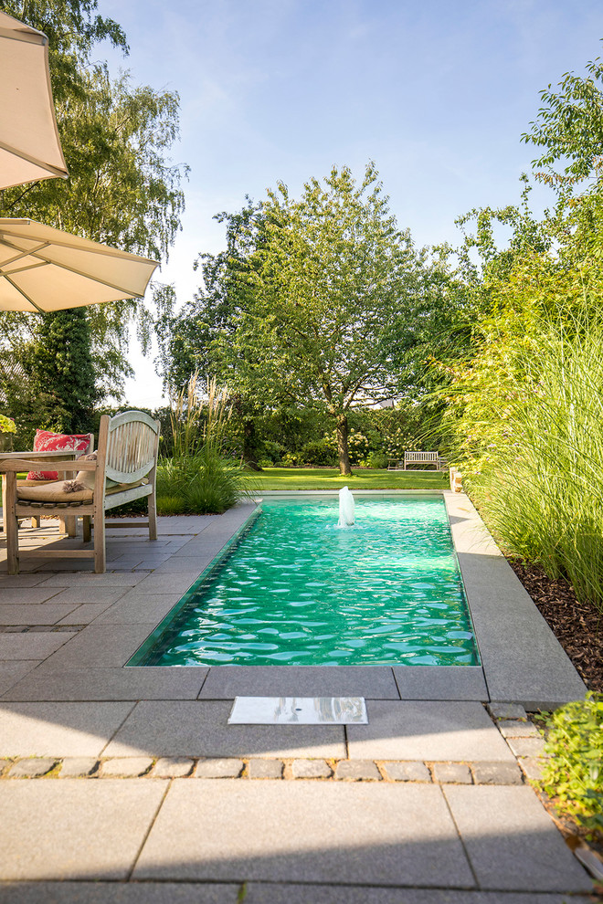 This is an example of a small contemporary backyard rectangular pool in Dusseldorf with a water feature and concrete pavers.