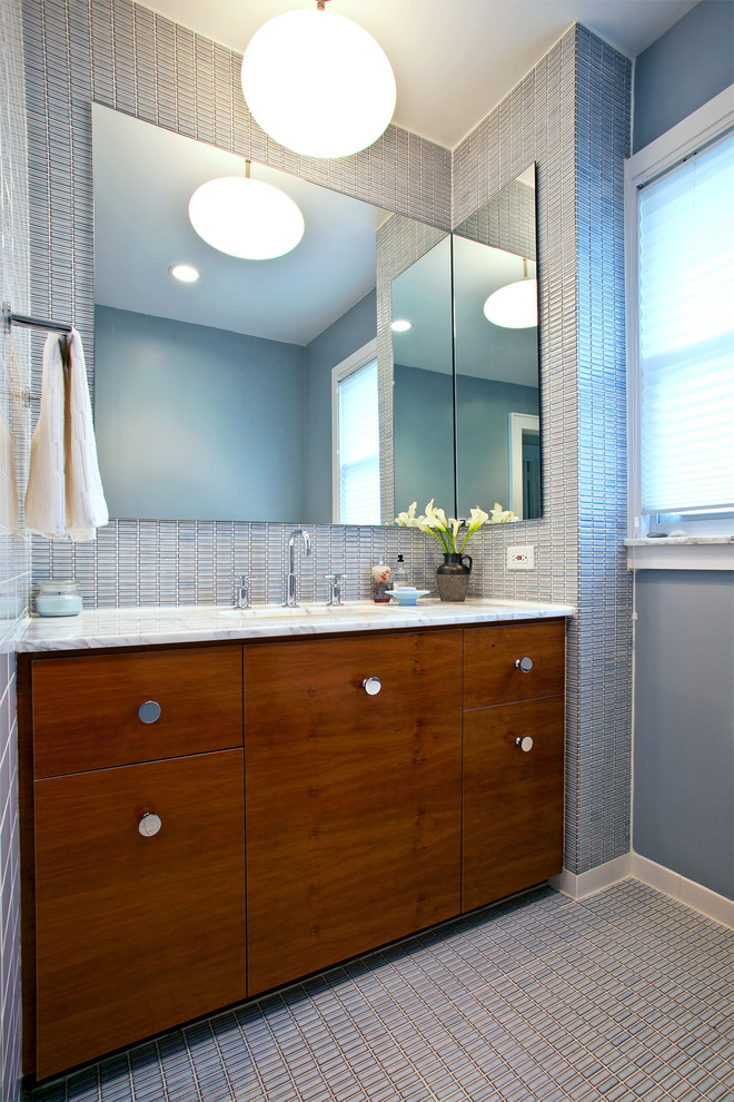 Photo of a large midcentury master bathroom in New York with an undermount sink, flat-panel cabinets, medium wood cabinets, marble benchtops, an alcove tub, a shower/bathtub combo, a one-piece toilet, blue tile, ceramic tile, blue walls, ceramic floors and blue floor.