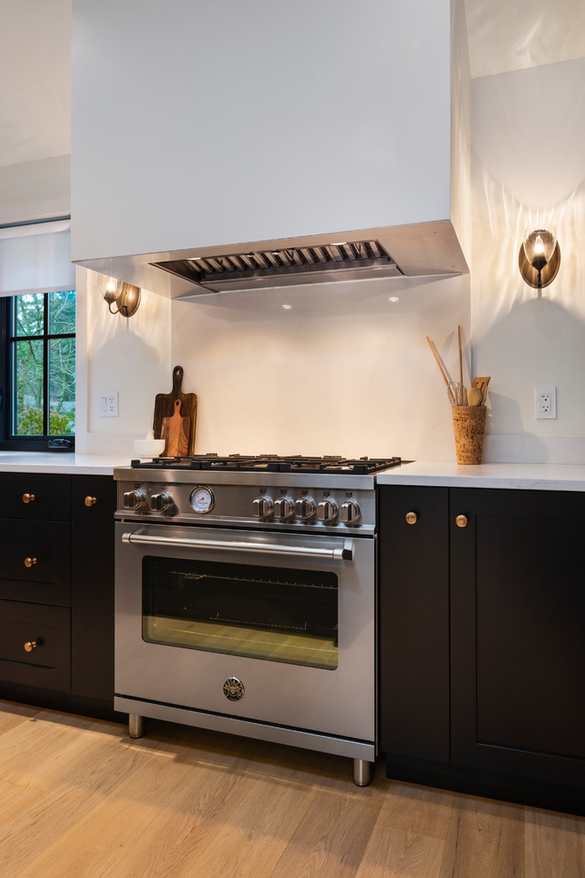 Inspiration for a mid-sized rustic l-shaped light wood floor and beige floor open concept kitchen remodel in Vancouver with a farmhouse sink, shaker cabinets, black cabinets, quartz countertops, paneled appliances, an island and white countertops