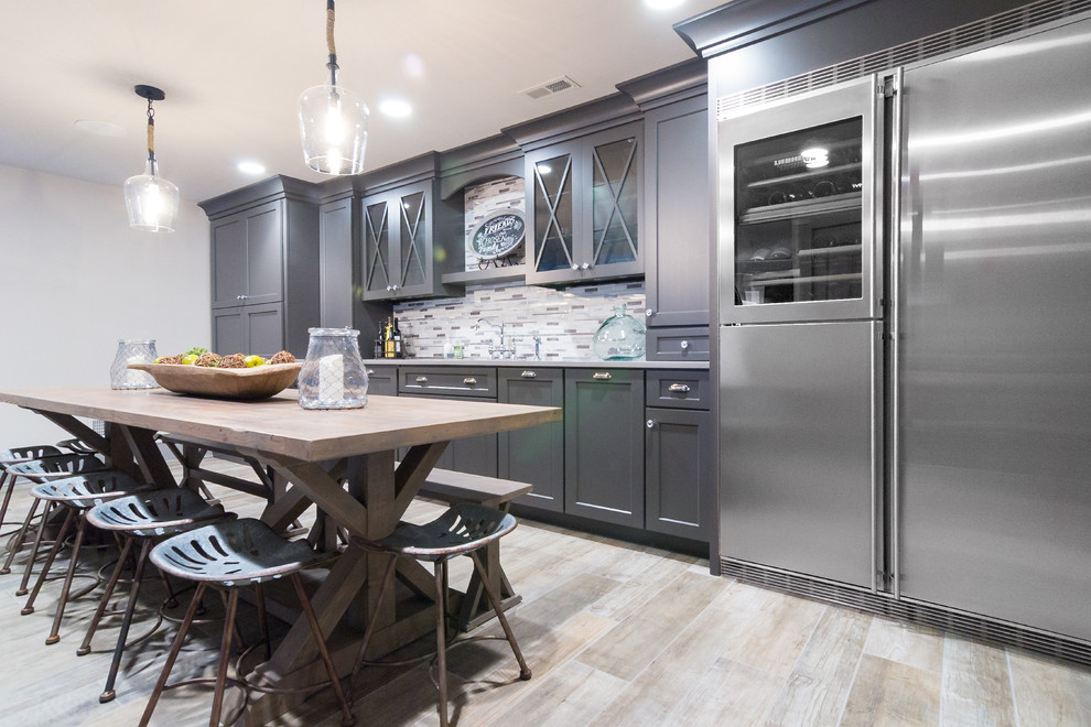 Inspiration for an expansive country single-wall wet bar in Philadelphia with an undermount sink, raised-panel cabinets, grey cabinets, quartz benchtops, multi-coloured splashback, glass tile splashback, laminate floors, beige floor and grey benchtop.