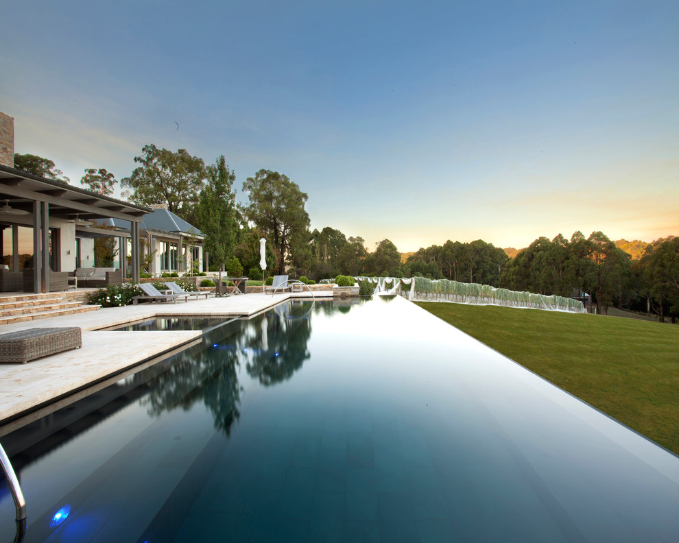 Design ideas for a large traditional rectangular infinity pool in Melbourne with natural stone pavers and a hot tub.