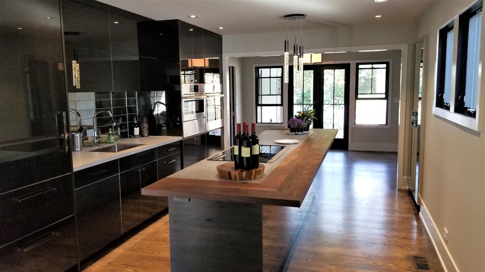 Open concept kitchen - mid-sized modern single-wall medium tone wood floor and brown floor open concept kitchen idea in Chicago with an undermount sink, flat-panel cabinets, black cabinets, metallic backsplash, mirror backsplash, stainless steel appliances, an island and quartz countertops