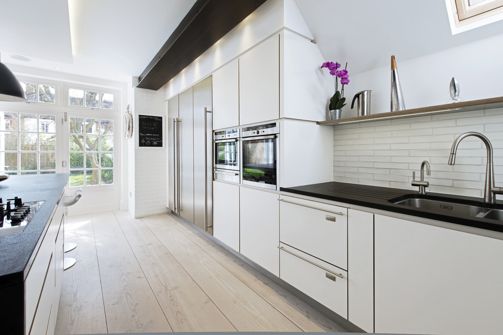 Design ideas for a scandinavian kitchen in London with flat-panel cabinets, light hardwood floors, with island, a double-bowl sink, white splashback and stainless steel appliances.