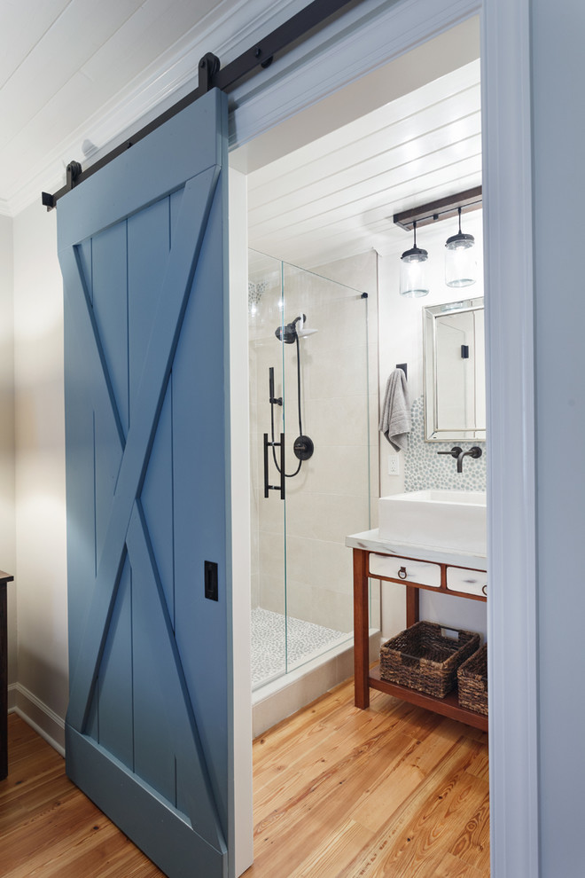 Inspiration for a country 3/4 glass tile medium tone wood floor and brown floor alcove shower remodel in Charlotte with brown cabinets, white walls, a vessel sink, a hinged shower door, marble countertops, white countertops and flat-panel cabinets