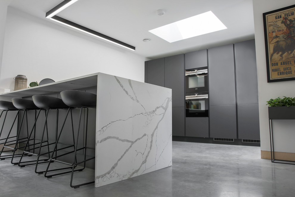 This is an example of a mid-sized contemporary u-shaped open plan kitchen in Essex with an integrated sink, flat-panel cabinets, grey cabinets, marble benchtops, white splashback, marble splashback, panelled appliances, concrete floors, a peninsula, grey floor and white benchtop.