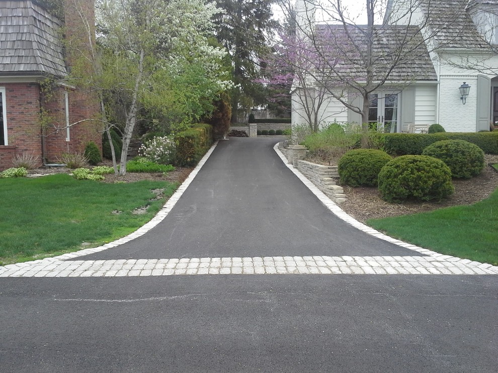 Photo of a mid-sized traditional front yard partial sun driveway in Chicago with a retaining wall and natural stone pavers.