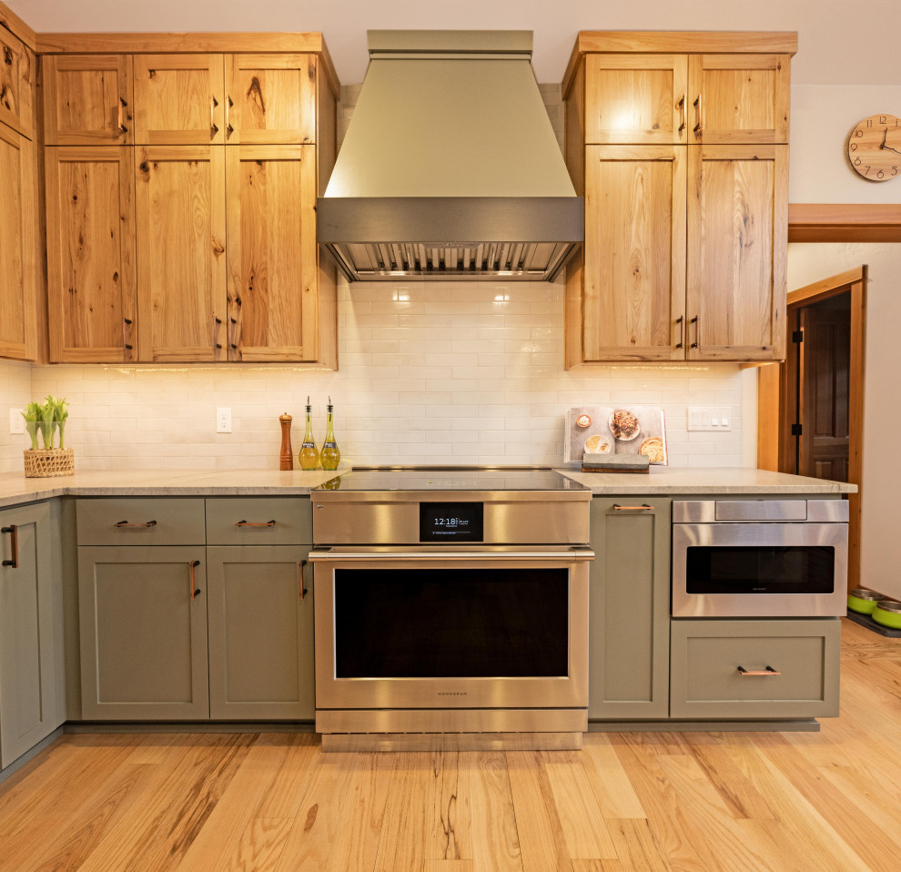 Example of a large mountain style u-shaped light wood floor and brown floor eat-in kitchen design with a farmhouse sink, shaker cabinets, quartzite countertops, gray backsplash, ceramic backsplash, stainless steel appliances, a peninsula and gray countertops
