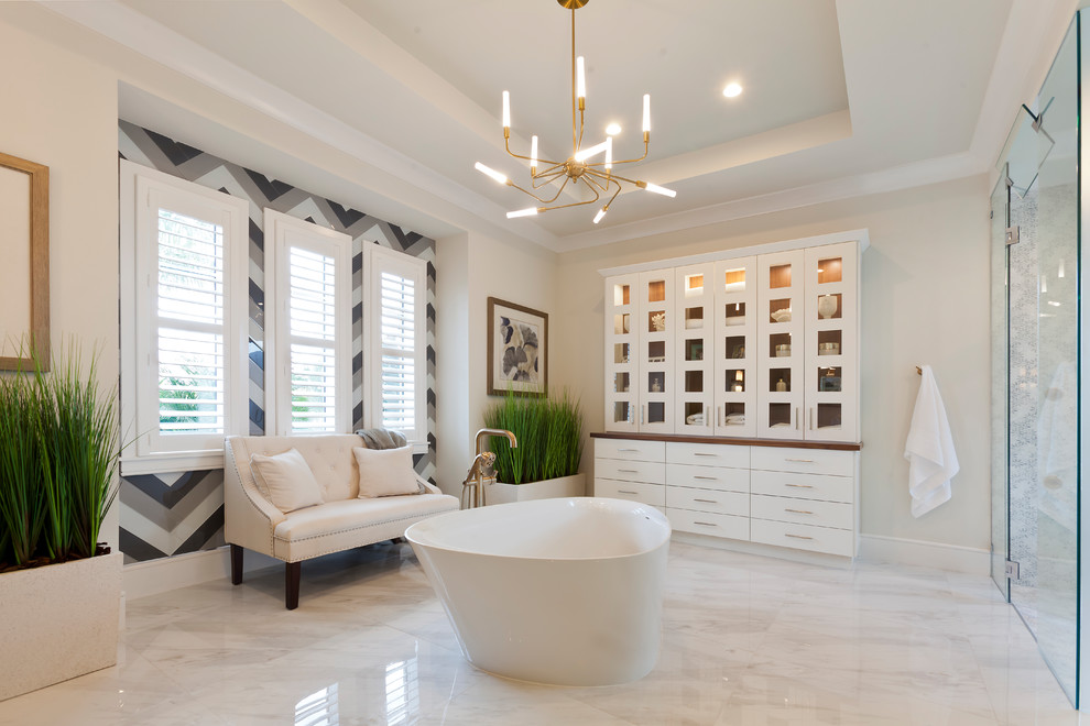 This is an example of an expansive transitional master bathroom in Tampa with flat-panel cabinets, white cabinets, a freestanding tub, a corner shower, a one-piece toilet, gray tile, subway tile, white walls, porcelain floors, a vessel sink, solid surface benchtops, multi-coloured floor, a hinged shower door and white benchtops.