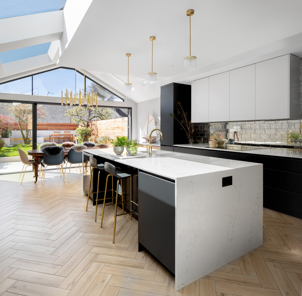 This is an example of a mid-sized modern eat-in kitchen in London with a single-bowl sink, flat-panel cabinets, black cabinets, metallic splashback, metal splashback, light hardwood floors, with island, beige floor and white benchtop.